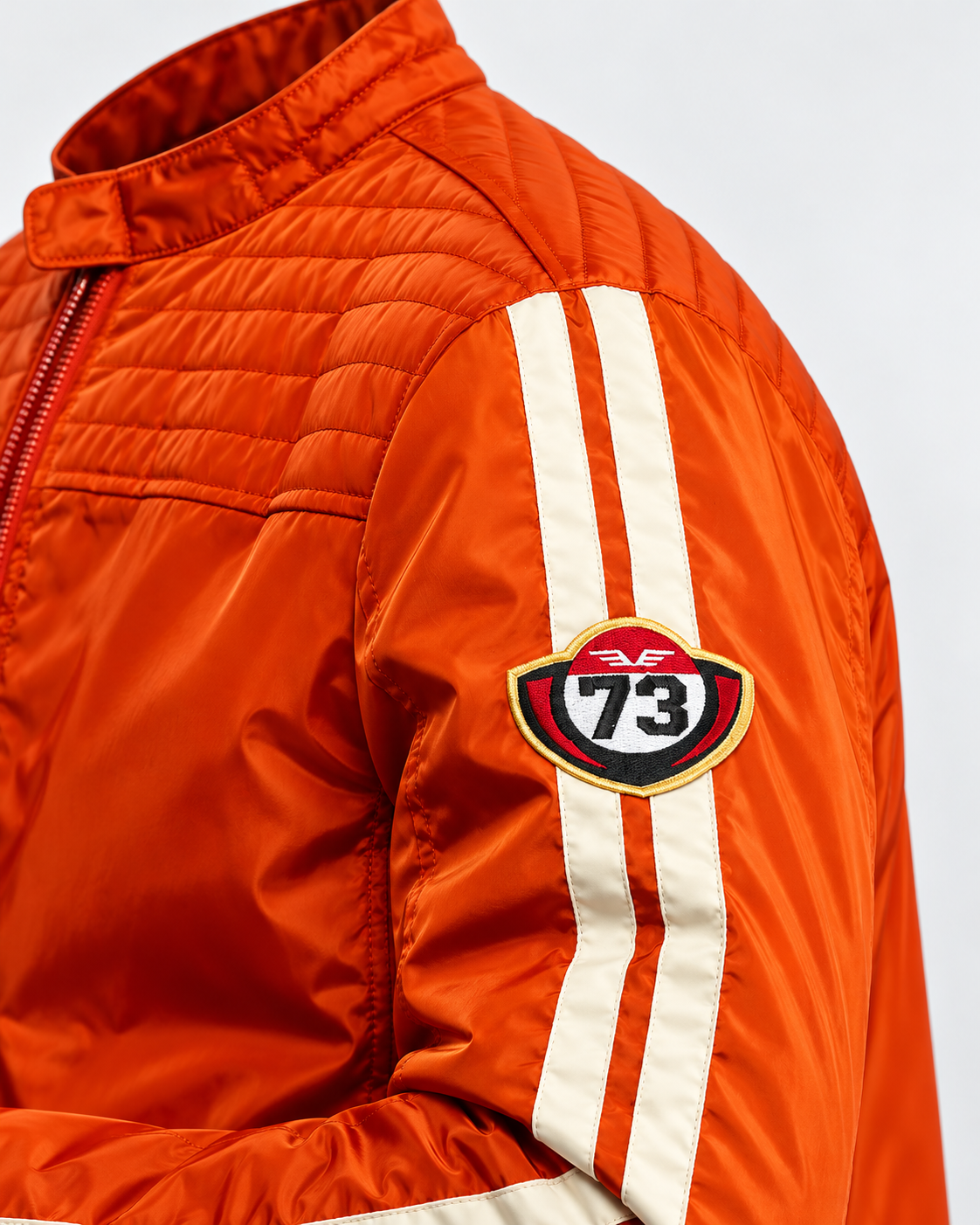 Détail veste racing orange avec écusson 73 brodé et bandes blanches sur la manche