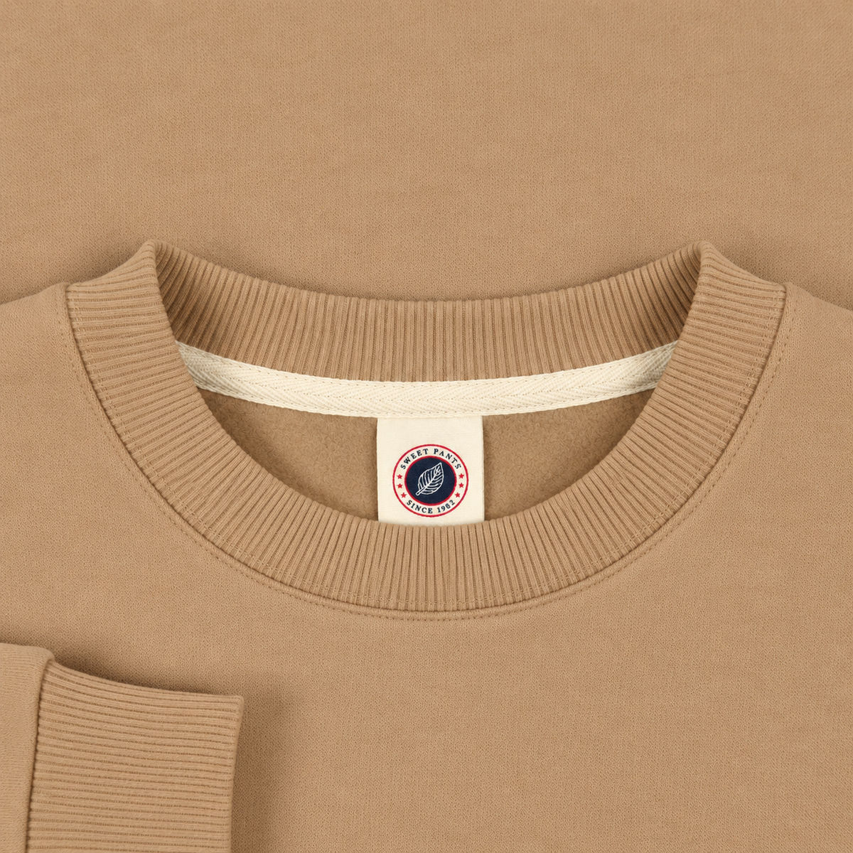Gros plan sur le col rond en bord-côte et l'étiquette Sweet Pants du sweat F Iconic Crew beige
